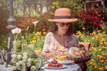 Téléchargez les photos : Photo de la femme heureuse mangeant des croissants dans le jardin pendant la journée ensoleillée. - en image libre de droit