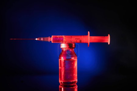 Foto de Primer plano de la jeringa con dosis de vacuna contra la infección por coronavirus y colocada encima del vial médico en un lugar oscuro - Imagen libre de derechos