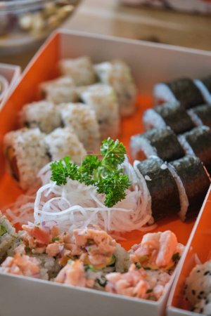 Foto de Desde arriba de deliciosos surtidos rollos de sushi fresco con daikon servido en caja de cartón con verduras en la cocina del restaurante - Imagen libre de derechos