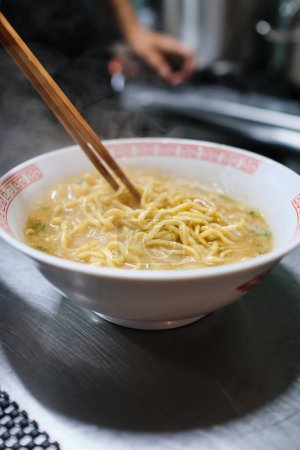 Photo for Closeup of traditional Japanese soup with herbs and noodles served in white bowl on metal table in kitchen - Royalty Free Image