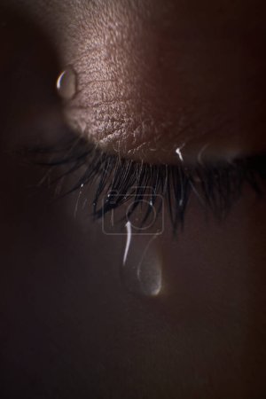 Photo for Closeup eye of crop unrecognizable sad person with tears on eyelid and eyelashes standing in murk room with dim light - Royalty Free Image