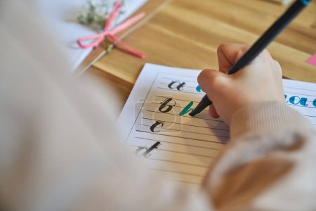 Photo for From above of anonymous person practicing lettering writing in lined notebook placed on wooden table using professional blue marker - Royalty Free Image