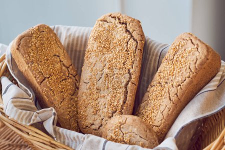 Foto de Panes largos de delicioso pan integral con semillas de sésamo en canasta de mimbre colocada sobre la mesa en la panadería - Imagen libre de derechos