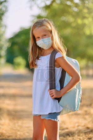 Photo for Portrait of girl in protective mask and with backpack standing on sunny day in countryside - Royalty Free Image