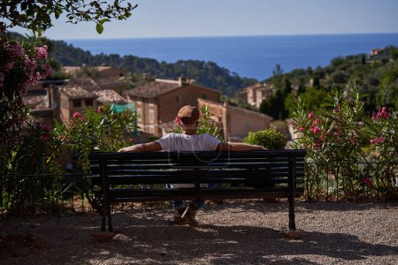 Photo for Back view of unrecognizable male tourist relaxing on bench and admiring picturesque scenery of old town and sea during summer trip - Royalty Free Image
