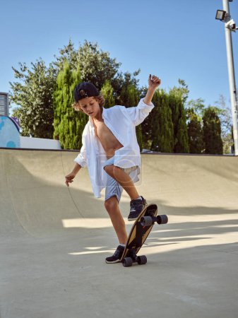 Photo for Full body side view of young boy skater in casual clothes balancing skateboard on street and looking down while practicing tricks during skate - Royalty Free Image