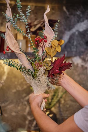 Téléchargez les photos : Cultiver femelle démontrant bouquet de fleurs séchées baies et branches d'eucalyptus dans la boutique de fleuristes - en image libre de droit