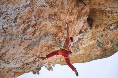 Foto de Desde abajo vista lateral del hombre fuerte alpinista en ropa deportiva colgando de la cuerda en las montañas rocosas - Imagen libre de derechos