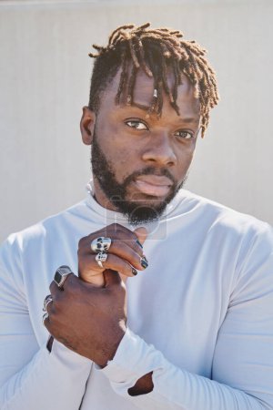 Photo for Portrait of thoughtful bearded African American man with dreadlocks wearing rings on fingers and looking at camera - Royalty Free Image