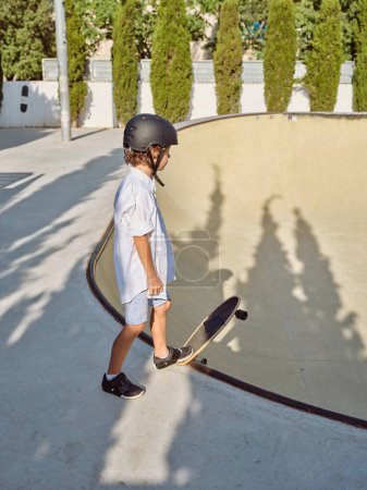 Photo for Side view full length of young skater standing with longboard on ramp edge and preparing to ride in skate park - Royalty Free Image