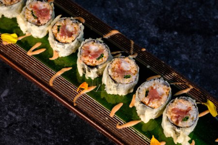 Téléchargez les photos : D'en haut de rouleaux de sushi assortis avec du poisson et du riz à la crème colorée servis sur un plateau en bois avec des fleurs sur une table en marbre à l'intérieur - en image libre de droit