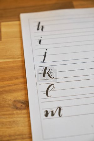 Photo for High angle of lined paper sheet with sequence of alphabet letters drawing steps placed on wooden table for lettering lesson - Royalty Free Image