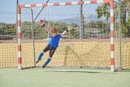Photo for Full body of preteen goalkeeper in sportswear jumping to side while catching ball during soccer training on sports ground - Royalty Free Image