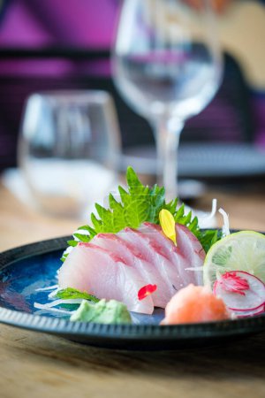 Photo for Tasty sashimi of yellowtail fish served with lime slice on wooden table with glassware on blurred background in light restaurant - Royalty Free Image