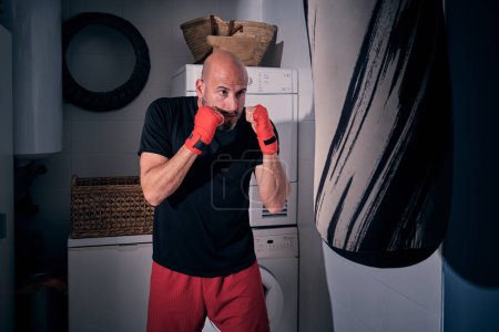 Téléchargez les photos : Entraînement de boxe dans la buanderie à la maison avec un sac et des gants - en image libre de droit