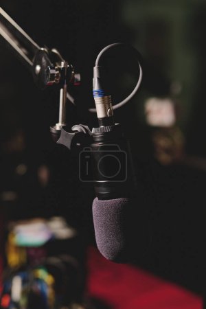 Téléchargez les photos : Microphone à condensateur professionnel contemporain placé sur fond flou du studio dans une lumière tamisée et prêt pour l'enregistrement de podcast - en image libre de droit
