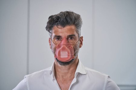 Photo for Portrait of man in white shirt wearing respirator and preventing spread of coronavirus by following quarantine restriction while standing on white background - Royalty Free Image