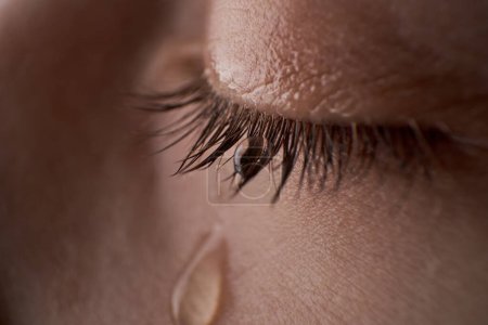 Photo for Closeup closed eye of crop anonymous unhappy crying kid with small tear rolling down on cheek while standing in light room - Royalty Free Image