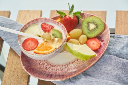 Foto de De arriba del tazón con yogur fresco cubierto con una variedad de rebanadas de frutas y bayas servidas en la mesa de madera en la cocina - Imagen libre de derechos