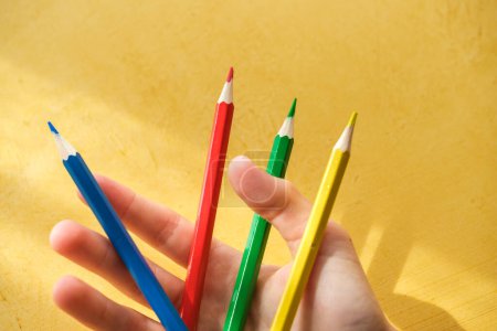 Téléchargez les photos : Ramassage à la main d'un enfantRamassage à la main d'un enfant de crayons de couleur sur fond jaune. Photo de haute qualité - en image libre de droit