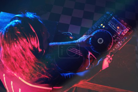 Foto de Desde arriba de DJ masculino anónimo en auriculares que reproducen música en el reproductor de CDJ mientras se realiza la canción en el moderno club nocturno oscuro - Imagen libre de derechos
