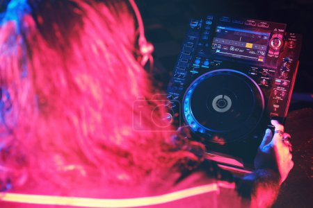 Foto de Desde arriba de DJ masculino anónimo en auriculares que reproducen música en el reproductor de CDJ mientras se realiza la canción en el moderno club nocturno oscuro - Imagen libre de derechos