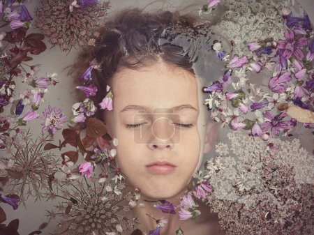 Téléchargez les photos : Vue du dessus du garçon mignon avec les yeux fermés couché dans la salle de bain avec de l'eau claire et de petites fleurs colorées dans la salle de bain - en image libre de droit