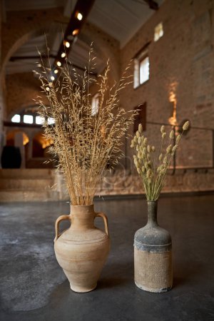 Téléchargez les photos : Tas de longues brindilles séchées dans de vieux vases d'argile placés sur le sol gris dans une pièce lumineuse avec un style à l'ancienne - en image libre de droit