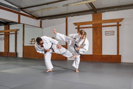 Téléchargez les photos : Deux personnes avec masque et kimono pratiquant le krav maga donnent des coups de pied lors d'un combat dans une salle de gym - en image libre de droit