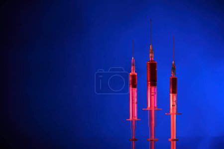 Photo for Closeup of medical syringes with needles filled with COVID19 vaccine and placed on reflective surface in neon lighting - Royalty Free Image