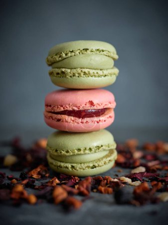 Photo for Tasty pistachio and strawberry macaroons placed on top of each other near dried fruit tea leaves against blurred gray background - Royalty Free Image