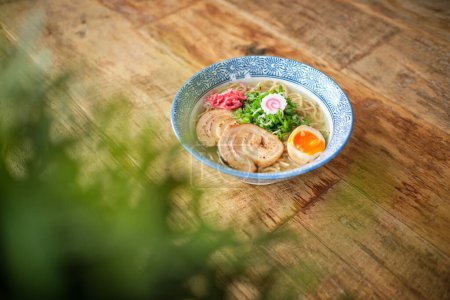Téléchargez les photos : D'en haut de délicieuse soupe ramen avec oeuf tendre bouilli et porc chashu servi dans un bol en céramique placé sur une table en bois sur fond flou - en image libre de droit