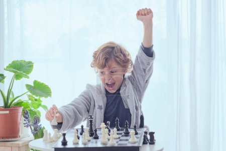 Photo for Happy preteen boy doing checkmate and showing fist up gesture with raised hand while winning chess game - Royalty Free Image