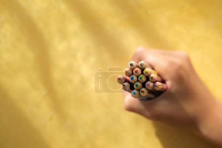 Téléchargez les photos : Ramassage à la main d'un enfantRamassage à la main d'un enfant de crayons de couleur sur fond jaune. Photo de haute qualité - en image libre de droit