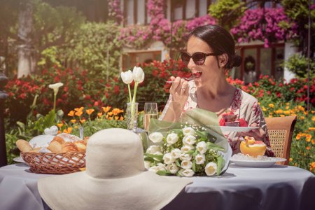 Téléchargez les photos : Photo de stock de femme heureuse appréciant le petit déjeuner dans le jardin pendant la journée ensoleillée. - en image libre de droit