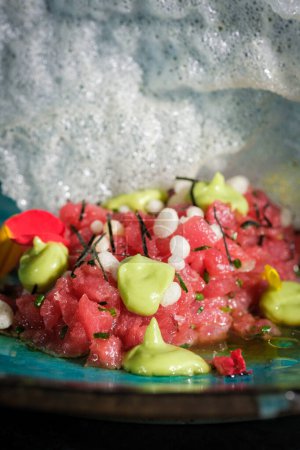 Foto de Tartar de atún crudo fresco y apetitoso servido con wasabi verde picante y hierbas en el plato con galleta de camarón blanco en el restaurante - Imagen libre de derechos