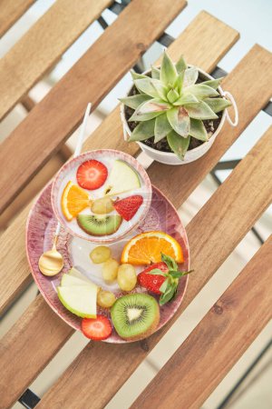 Photo for From above of various healthy fruits and berries in bowl with tasty yogurt placed on wooden table during breakfast in kitchen - Royalty Free Image