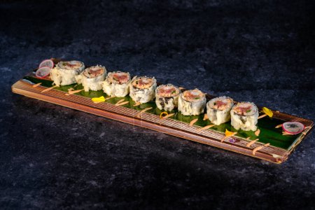 Foto de Desde arriba de surtidos rollos de sushi con pescado y arroz con crema colorida servida en bandeja de madera con flores sobre mesa de mármol en el interior - Imagen libre de derechos