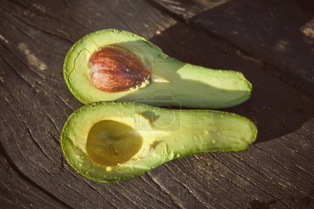 Photo for From above of halves of fresh green avocado with seed placed on wooden table on sunny day - Royalty Free Image
