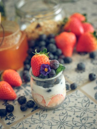 Photo for High angle of jar with yummy yogurt with ripe strawberries and blueberries served on table for breakfast at home - Royalty Free Image