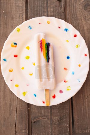 Foto de Desde arriba plato blanco decorado festivo y helado con símbolo LGBT en palo sobre fondo de madera - Imagen libre de derechos