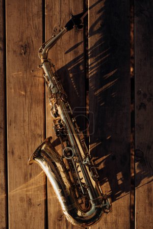 Photo for Golden saxophone lying on an old wood shining in the sunlight - Royalty Free Image