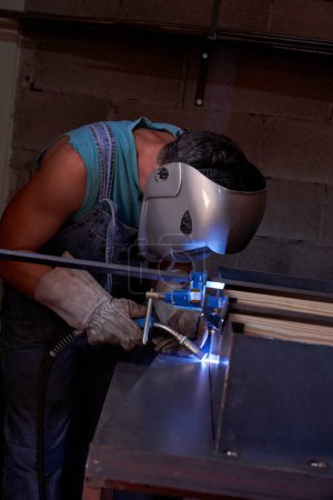 Photo for Side view of faceless male worker in protective mask making welding seams on metal structure with special equipment during work in professional workshop - Royalty Free Image