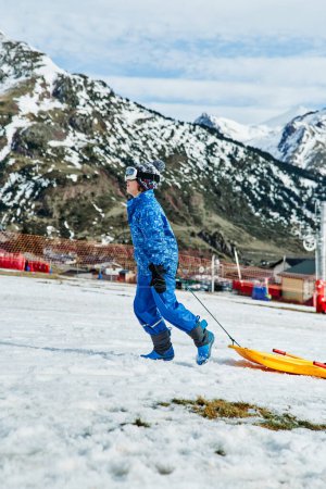 Photo for Side view of boy with plastic sledge walking up snowy slope while spending time on sunny winter day in highlands - Royalty Free Image