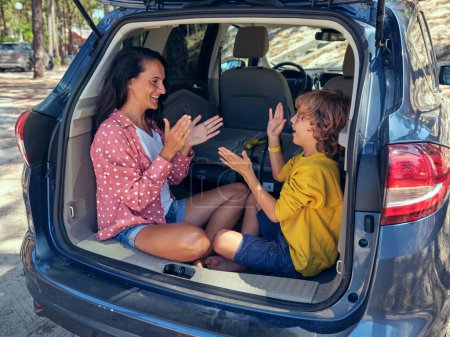 Photo for Positive mother with son playing Pat a cake game and looking at each other while sitting in truck of car parked in countryside on summer day - Royalty Free Image
