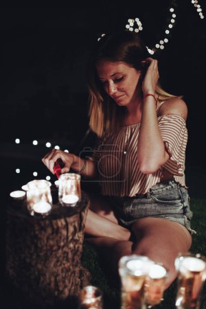 Foto de Mujer encendiendo velas en jardín oscuro - Imagen libre de derechos