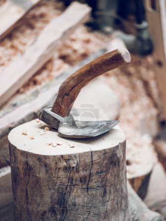 Foto de Herramienta retro adze con borde de corte y mango de madera para tallar madera colocada sobre un muñón de madera con afeitado en el campo - Imagen libre de derechos