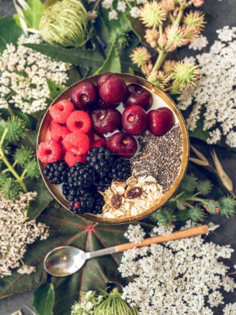 Photo for From above of ripe berries placed in bowl on table with plants and spoon in daytime - Royalty Free Image