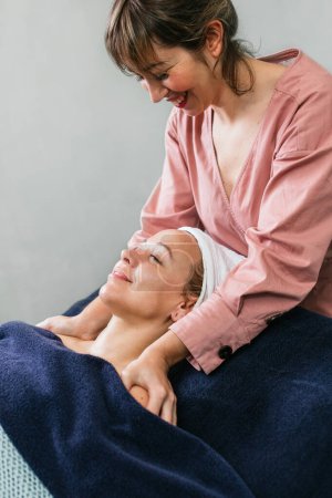 Téléchargez les photos : Contenu masseuse massant les épaules d'une cliente allongée sur la table dans un salon de beauté - en image libre de droit