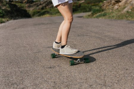 Photo for Cropped unrecognizable young female riding longboard on asphalt road between hills under cloudy sky - Royalty Free Image